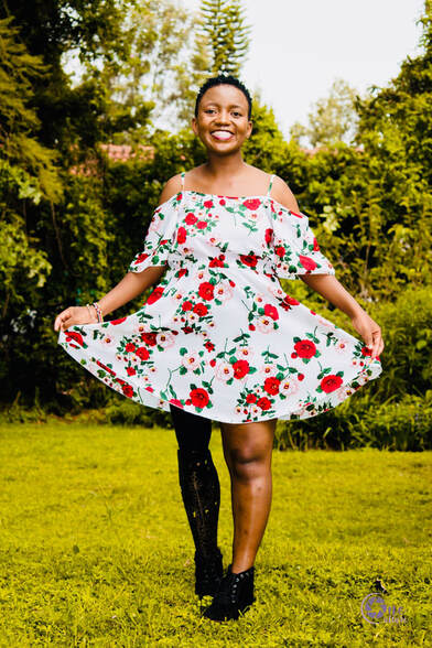 Young black woman standing outside smiling holding out the hem of her dress showing prosthetic leg